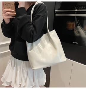 Detailed view of cream PU leather tote bag held by model in casual interior setting