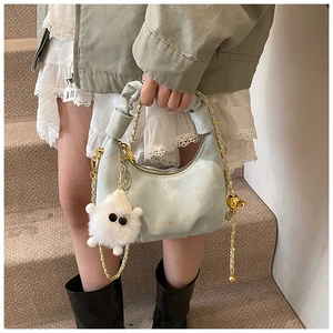 Detail of mint green pleated half-moon bag with gold chain and white fuzzy monster charm
