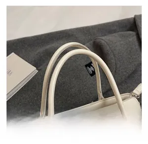 Détail du sac à main crème montrant les anses arrondies et le fermoir rotatif en argent
