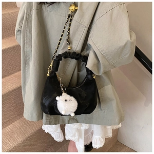 Détail du sac noir avec poignée plissée et breloque en forme de mouton en peluche