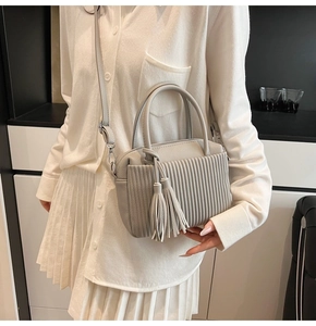Detail of light gray lychee grain leather bag with elegant pleated texture and long tassels