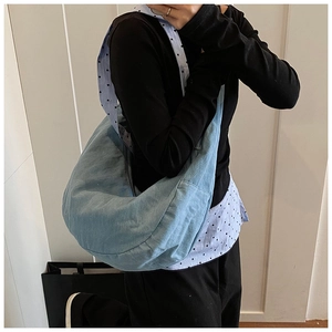Détail d'un grand sac hobo en jean bleu clair porté à l'épaule par un mannequin de mode