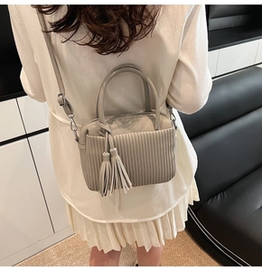 Detail of grey pleated shoulder bag with tassel pendants and adjustable strap