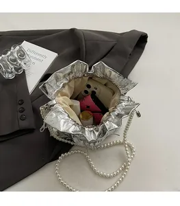 Interior view of silver pleated bucket bag with pearl chain showing phone and lipstick