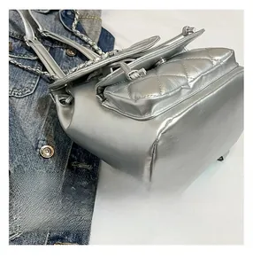 Macro view of silver quilted backpack featuring metallic chain and leather drawstring detail