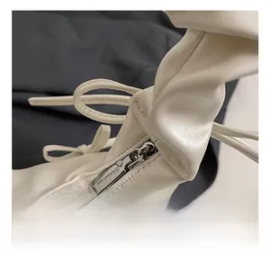 Detail of minimalist beige pleated handbag showing silver zipper and ribbon bow decoration