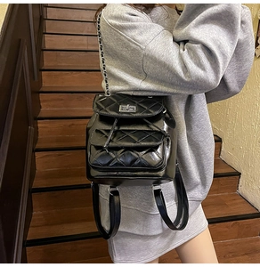 Close-up of black quilted leather backpack with silver chain and glossy finish on stairs