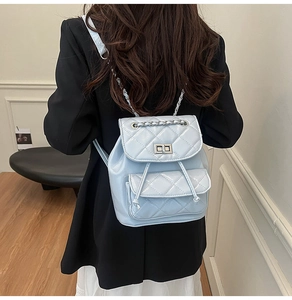 Rear view of a model wearing a light blue quilted backpack with chain straps