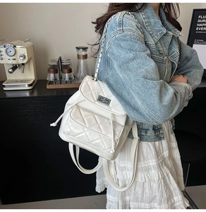Detail view of white quilted faux leather backpack with chain straps and metal twist lock