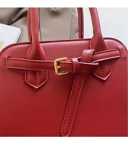 Close-up of red matte leather tote showing golden metal buckle and stitching detail