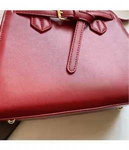 Macro shot of dark red leather texture and precise stitching on tote bag with gold buckle