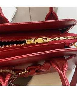 Detailed close-up of the polished gold hardware and smooth red leather tote bag