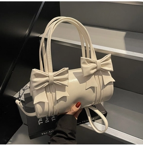 Detailed view of cream bow cylinder bag with glossy finish and detachable strap