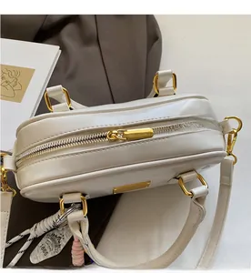 Nahaufnahme des goldenen Metallreißverschlusses und der Doppelgriffe der beigen Handtasche