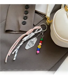 Detail eines bunten Perlenanhängers mit geflochtenem Seil an einer weißen Tasche