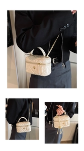 Detail of a beige quilted crossbody box bag with gold floral clasp and chain strap