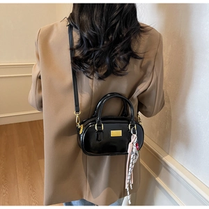 Nahaufnahme einer glänzend schwarzen Mini-Bowlingtasche mit Goldplakette und Web-Anhänger