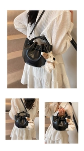 Detailed shot of a chic black leather bucket handbag with woven handle and cute puppy charm.