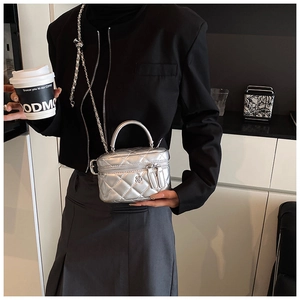 Detail of silver quilted mini box bag with metal handle and detachable chain strap