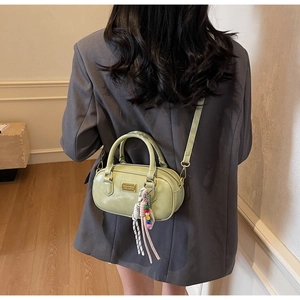 Detail der hellgrünen Boston-Tasche mit Perlenanhänger über grauem Blazer