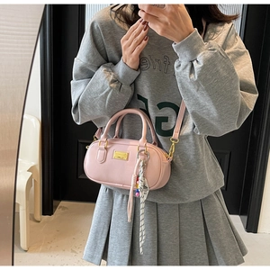 Détail du sac Boston rose clair avec logo doré, écharpe rayée et pendentif en perles