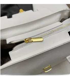 Close-up of smooth gold metal zipper and white leather texture on handbag top