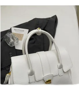 Close-up of white leather handbag with gold metal lock and durable dual handles