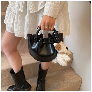 Close-up detail of the stylish black bucket bag featuring unique twisted handle and cute plush charm.