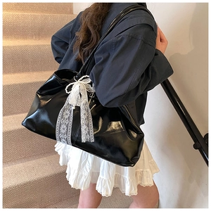 Detail of black glossy tote bag featuring white lace bow and elegant pearl charms