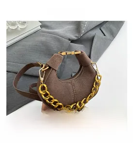 Detalle de bolso medialuna de ante marrón con cadena dorada y cierre metálico elegante