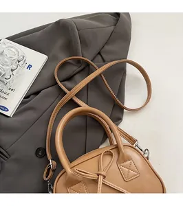 Borsa bowling marrone con dettaglio fiocco su sfondo di giacca sartoriale grigia
