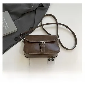 Détail d'un petit sac bandoulière marron en similicuir avec surpiqûres et boucle argentée