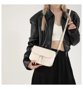Détail d'un sac à bandoulière crème minimaliste porté avec une veste en cuir