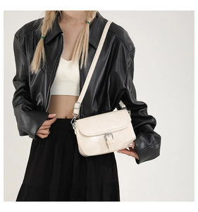 Sac bandoulière crème avec boucle argentée porté sur une veste en cuir noir chic