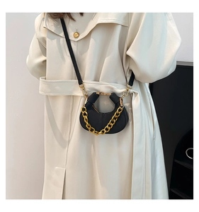 Detalle de mini bolso medialuna negro con cadena dorada gruesa sobre gabardina beige