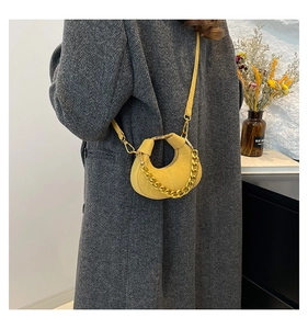 Detalle del bolso de media luna amarillo con cadena dorada sobre un abrigo de lana gris