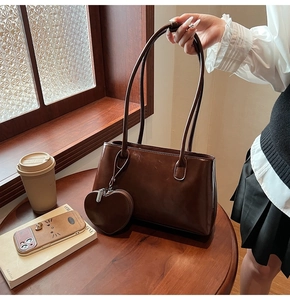 Detail of dark brown patent leather tote bag with heart charm on a wooden table