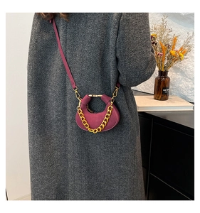 Bolso de media luna color ciruela con cadena dorada sobre un abrigo gris elegante