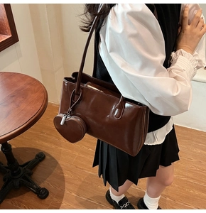 Detail of dark brown patent leather hobo bag with a heart charm in a cafe setting