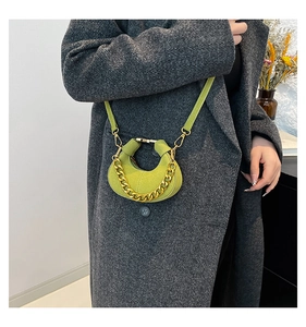 Bolso media luna verde con cadena dorada sobre un abrigo gris de espiga elegante