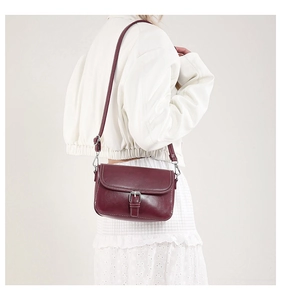 Détail macro du sac bandoulière rouge vin avec surpiqûres blanches et boucle en argent