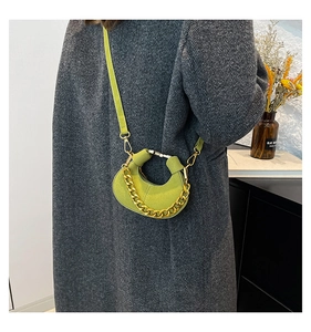 Detalle de bolso medialuna de ante verde con cadena dorada sobre abrigo de espiga