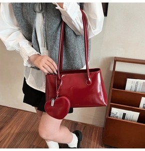 Close-up of wine red patent leather shoulder bag with a heart-shaped charm accessory