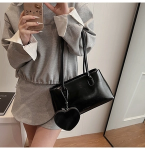 Black glossy leather tote bag with a heart charm and slim shoulder straps on a model