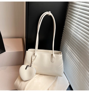 Detail of cream white leather shoulder bag with a small heart shaped coin purse charm