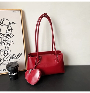 Détail d'un sac bandoulière en cuir verni rouge avec une breloque cœur et fermeture éclair
