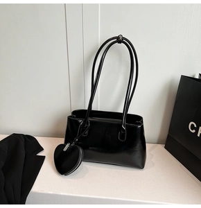 Detailed close-up of glossy black leather shoulder bag with a heart-shaped charm accessory