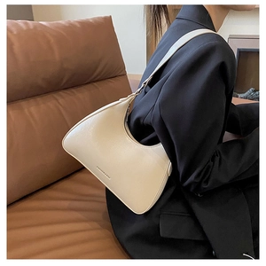 Detail of a creamy white moon-shaped hobo bag on a model shoulder with textured leather