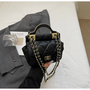 Detail of black quilted leather bag featuring gold semi-circular handle and turn-lock closure
