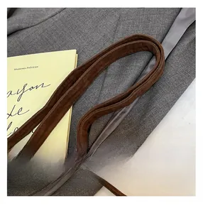 Détail de la bandoulière en daim marron foncé avec boucle en métal doré et surpiqûres